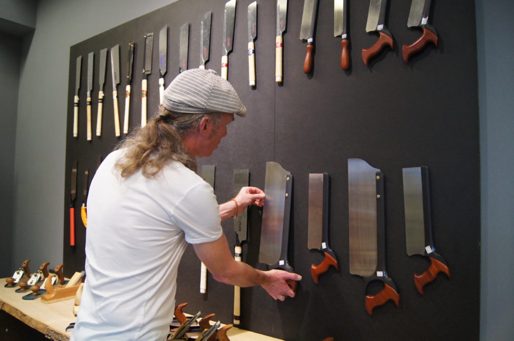 Manne steht vor einer Werkzeugwand mit Handsägen im Laden von Dieter Schmid